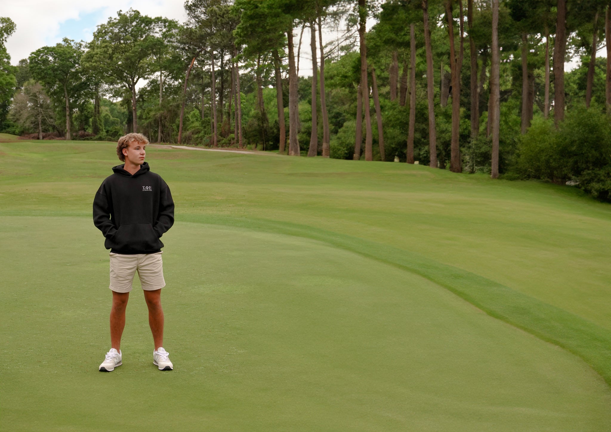 Blonde teenager standing on the green of a golf course with pine trees in the background
